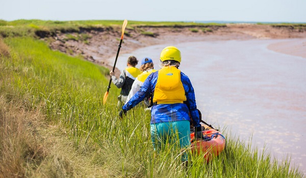 Students with a kayak walking toward a river near Minas Basin