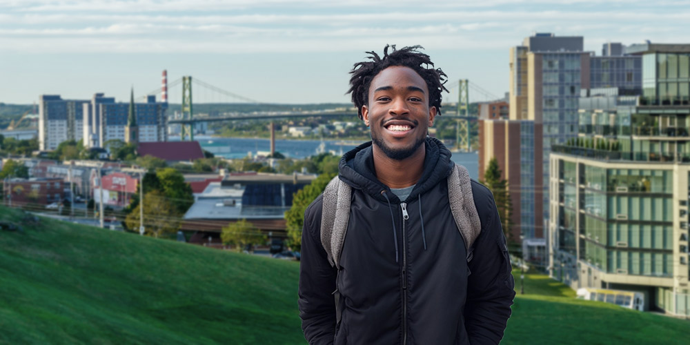 A young man in a hoodie is standing on Citadel Hill with the Halifax skyline behind him.